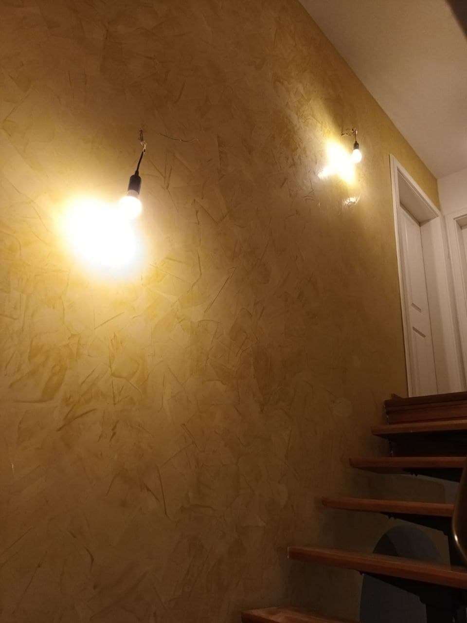Treppenhaus mit warm goldener Lasurfläche und zwei einfachen Wandleuchten