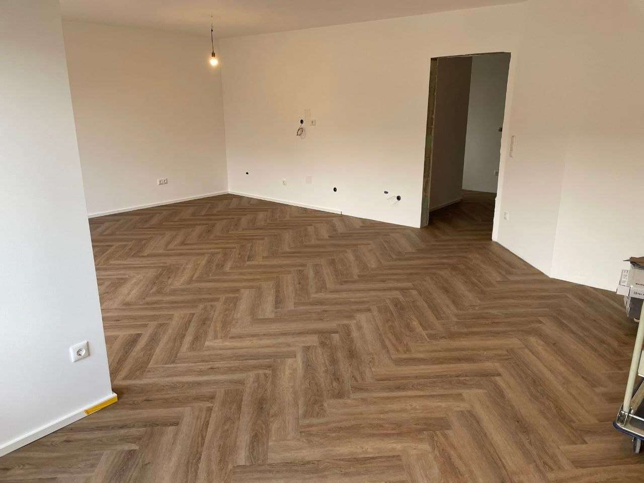 Fertig gestrichener Wohnraum mit hellen Wänden, Decke und Fischgrätboden