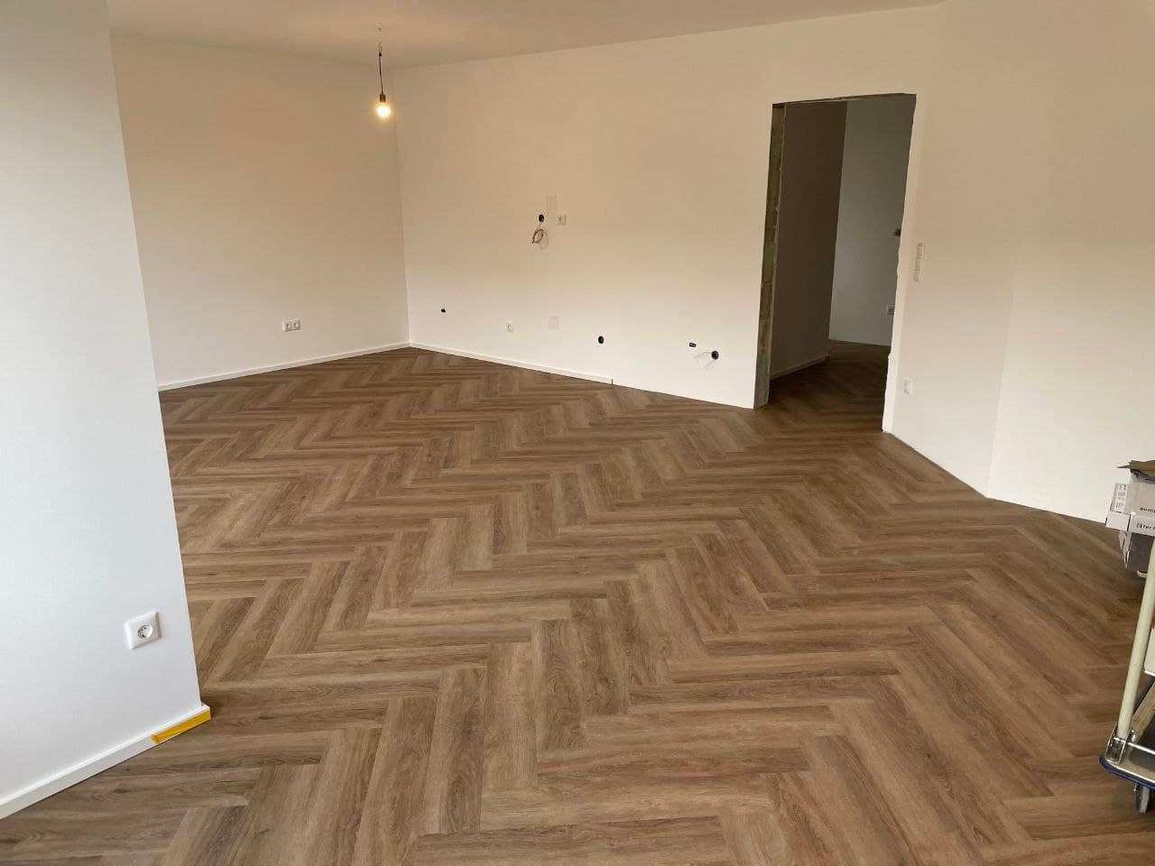 Leerer Wohnraum mit frisch gestrichenen Wänden, weißer Decke und Fischgrätboden
