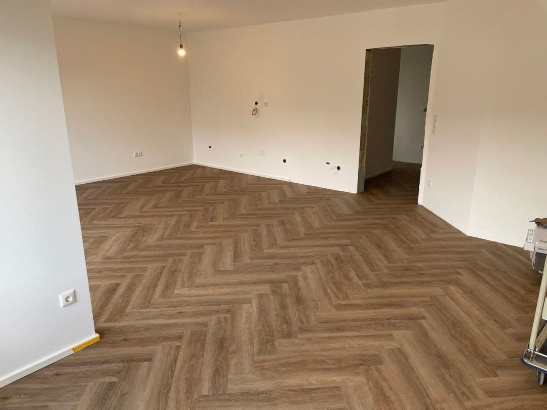 Fertig gestrichener Wohnraum mit hellen Wänden, Decke und Fischgrätboden